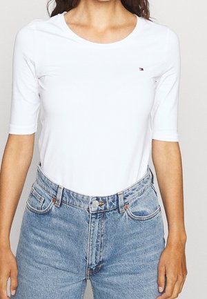 Witte T-shirt met korte mouwen en een ronde hals, gecombineerd met lichtblauwe denim jeans met hoge taille en koperen accenten.