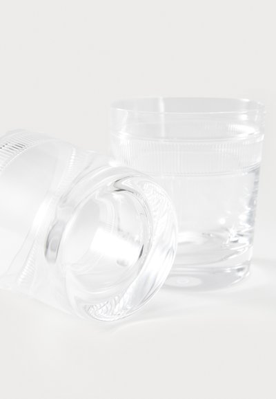 Dva prozorna steklena kozarca, eden postavljen pokončno, drugi prevrnjen, z gladkimi površinami in rahlimi teksturiranimi poudarki okoli robov.