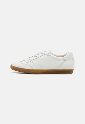 Hvid lavtop læder sneaker med brun gummisål, snørelukning og syninger på en ensfarvet lys baggrund.