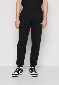 Svarta träningsbyxor i bomull med elastiskt midjeband, har en liten vit Nike-logotyp på vänster höft och smalnande mudd.