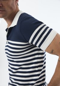 Marineblå og hvid stribet polo t-shirt med korte ærmer og ribbet krave. Har knaplukning og tekstureret stof.