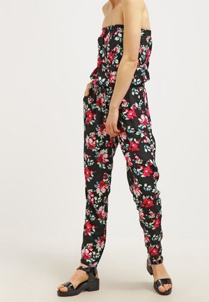 Mono negro sin tirantes con estampado floral en rojo, rosa y blanco, combinado con sandalias de tacón bloque abiertas en color negro.