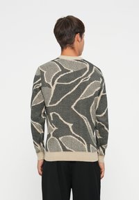 Gebreide trui met een zwart en beige abstract bladerenpatroon, ronde hals, lange mouwen en ribgebreide manchetten. Zachte textuur.