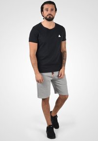 Zwarte katoenen t-shirt met een wit driehoeklogo, gecombineerd met grijze sportshorts met een verstelbarekoord en zijzakken.
