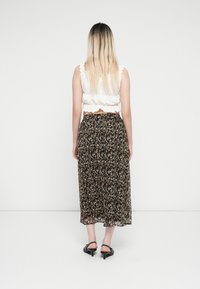 Schwarz-gestreifte Maxi-Rock mit floralem Muster und transparenter Textur, kombiniert mit einem weißen cropped Top mit Rüschenkanten und einem Rückenausschnitt.