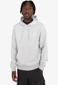 Sudadera con capucha de color gris claro, con un bolsillo tipo canguro y cordones. Presenta un pequeño logo en el pecho. Tejido suave y texturizado.