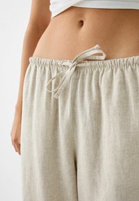 Béžové lněné kalhoty s stahovací šňůrkou v pase. Tkanina má jemnou texturu s lehkými horizontálními pruhy. Elastický pas pro pohodlí.