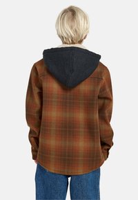 Camicia a quadri marrone e arancione con cappuccio grigio scuro, dotata di un sottile rivestimento e di una vestibilità comoda. Cuciture visibili e dettagli ai polsi.