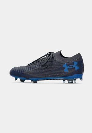 Chuteira de futebol cinza escuro e azul com atacadores, parte superior texturizada e cravos moldados na sola, vista lateral sobre um fundo branco.