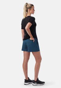 Svart kortärmad skjorta, blå shorts med sidfickor och svarta sportskor. Slätt tyg och avslappnad passform. Inga mönster eller logotyper synliga.