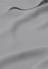 Hellgrauer Stoff mit einer glatten Textur, der das Licht subtil reflektiert. Er weist ein Fischgrätenmuster auf, das einen weichen, eleganten Look erzeugt.