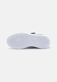 Semelle en caoutchouc blanche avec un motif de grip texturé et le logo "PUMA". La tige présente un mélange de couleurs et de matériaux, avec un design de sangle sécurisé.