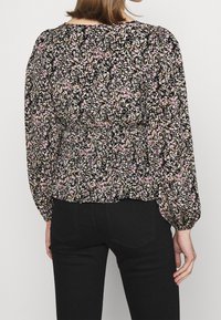 Blommig blus med svart bas, prydd med rosa, vita och gröna blommönster. Långa ärmar, rynkad midja och rund halsringning.