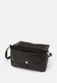 Czarna skórzana torba na ramię z otwartą klapą, srebrnym zapięciem magnetycznym, regulowanym paskiem oraz widoczną podszewką z materiału.