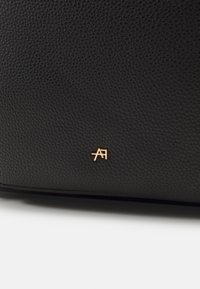 Svart texturerad läderväska med ett litet guldemblem med "AF"-logotypen i det nedre hörnet. Enkelt design med minimala hårdvaruaccents.