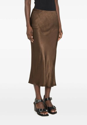 Donna con gonna midi in raso marrone abbinata a tacchi a blocco neri con punta aperta e doppi cinturini con fibbia.