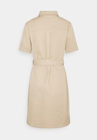 Robe chemise beige à manches courtes avec col, ceinture à la taille et détail de pli au dos, vue de dos sur fond blanc uni.