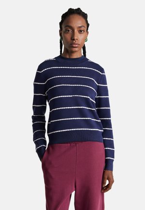 Sweter w granatowe paski z białymi poziomymi liniami, okrągłym dekoltem i długimi rękawami, zestawiony z burgundowymi spodniami. Gładka tekstura materiału.