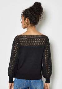 Czarny sweter z koronkowymi panelami na rękawach i plecach, z prążkowanymi mankietami i dołem. Koronka ma kwiatowy wzór, co dodaje tekstury.