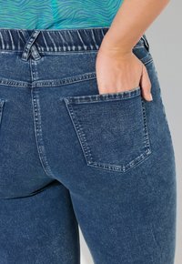 Denimjeans med elastisk midja, mörkblå färg, något urtvättad textur och en bakficka som detalj.