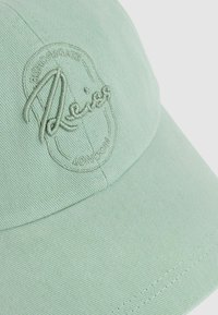 Green cotton baseball cap featuring embroidered logo detail, structured design, and curved visor. Texture is smooth with a subtle sheen.
