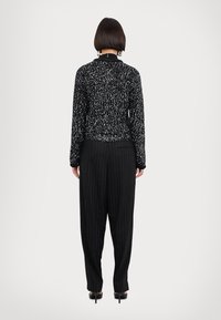 Maglia nera a maniche lunghe con un motivo marmorizzato, abbinata a pantaloni a strisce a vita alta; tessuto elegante, vestibilità rilassata e leggero luccichio.