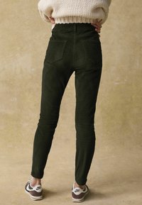Hoge taille groene corduroy broek met een slim fit, voorzien van twee achterzakken, gecombineerd met bruin-witte sport sneakers.