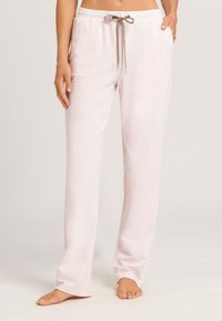 Lichtroze loungebroek van zacht materiaal, voorzien van een elastische tailleband en een decoratieve trekkoord met een bruine accenten.