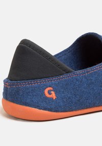 Pantofola di feltro blu con upper in tessuto nero, suola in gomma arancione e cucitura arancione. Presenta una lettera 'G' prominente di lato.