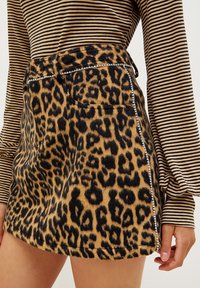 Mini gonna con stampa leopardata realizzata in tessuto morbido con macchie nere su sfondo beige. Presenta tasche laterali e cuciture decorative in argento.