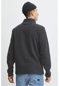 Temno siva flis pulover z visokim ovratnikom in rebrastim detajlom na hrbtu. Uporabljeno z svetlo modrimi kavbojkami.