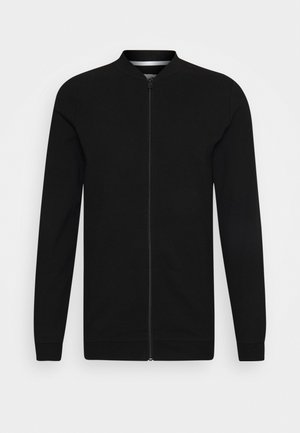 Czarna kurtka na zamek z długim rękawem wykonana z fakturowanej tkaniny, z prążkowanymi mankietami, kołnierzem i dołem, na jednolitym jasnym tle.