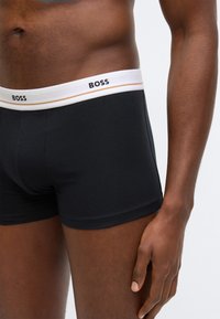 Boxeri negri din bumbac cu talie albă pe care este inscriptionat "BOSS" și o singură dungă orizontală accentuată. Textură netedă.