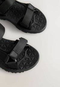 Svarta sandaler med en texturerad, diamantmönstrad sula, justerbara tygremmar och plastspännen för en säker passform.