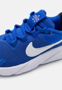 Blauer Sportschuh mit strukturiertem Obermaterial, weißem Swoosh-Logo und verstärkten Schnürsenkeln. Verfügt über eine gepolsterte Sohle und gemusterte Akzente.