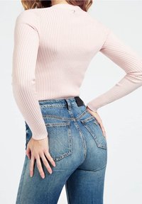 Světle růžový žebrovaný dlouhý rukáv tričko v kombinaci s úzkými modrými džíny. Džíny mají tradiční design kapes a černou nášivku na pasu.
