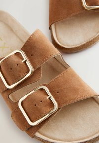 Sandale din suede maro, cu două bretele late, catarame aurii și talpă conturată. Textură moale și design cu vârful deschis.