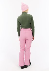 En grøn langærmet top parret med lyserøde bukser med lynlåse ved anklerne. En lyserød hue fuldender outfittet.