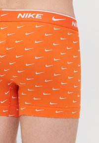 Narancssárga pamut boxer alsónadrág fehér Nike logó mintával. Az elasztikus derékpánton vastag fehér betűkkel szerepel a "NIKE" felirat. Simogató tapintás.