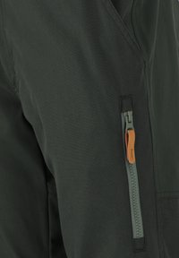 Mörkgrön tyg med en slät textur har en sidoficka med blixtlås och en läderdragning samt kontrasterande blixtlåsdetalj.