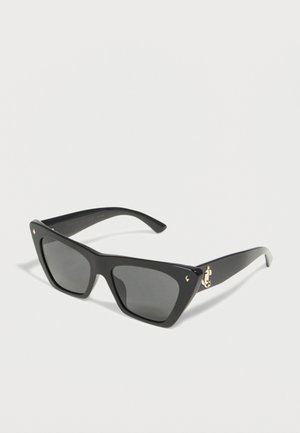 Svart oversized kvadratiske solbriller med mørke glass og gullfargede hengseldetaljer på hvit bakgrunn.