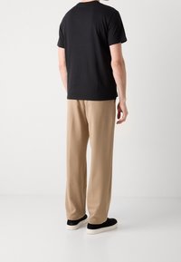 Czarna bawełniana koszulka i beżowe spodnie z miękkiego materiału. Czarne sneakersy z białymi podeszwami. Prosta, nieozdobna i luźna sylwetka.