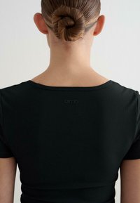 Top corto de manga corta negro con cuello redondo y un sutil detalle del logo en la parte posterior. Textura suave y diseño ajustado.