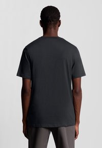 T-shirt nera a maniche corte con scollatura rotonda, texture liscia e vestibilità comoda, vista da dietro.