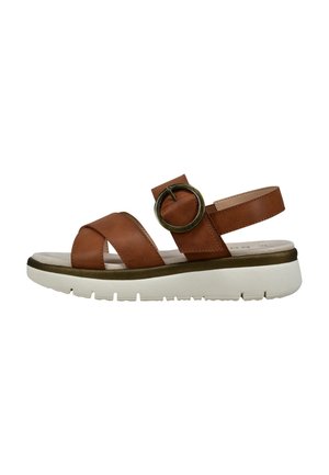 Brown leather sandal with cross straps, a circular accent, and a white textured sole. Includes a cushioned footbed for comfort.