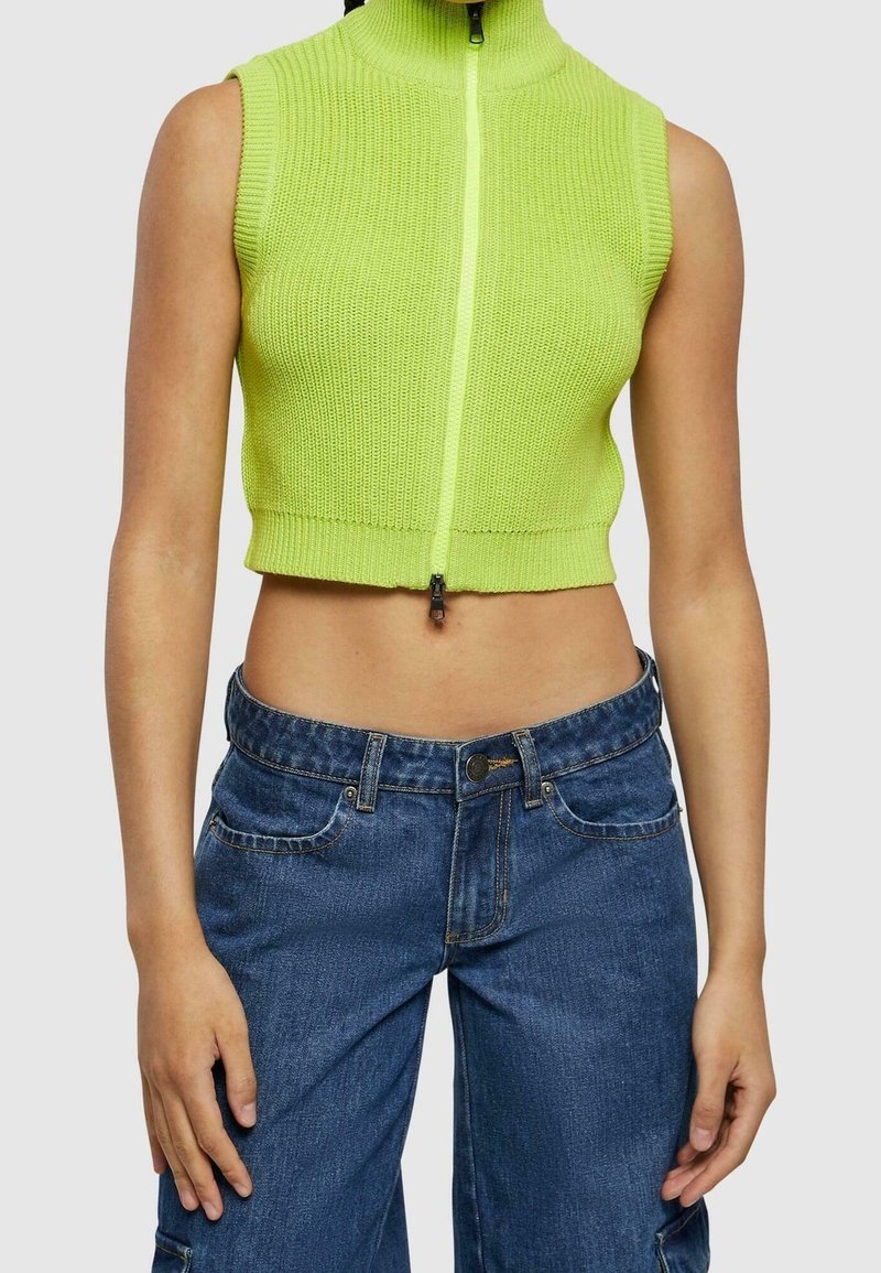 Top de punto corto en verde neón con cuello alto y cremallera frontal, combinado con pantalones vaqueros de pierna ancha en azul denim que cuentan con bolsillos delanteros.