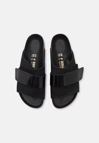 Infradito neri con design a bande incrociate, realizzati in suede e materiale sintetico, con una fascia regolabile nera lucida e una soletta sagomata.