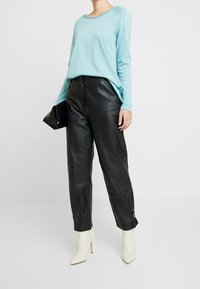 Light blue long-sleeve top paired with black leather pants and white high-heeled boots, held black clutch, on a neutral background.
