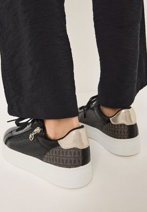 Sneaker neri e grigi con design testurizzato, accenti metallici dorati sul tallone e suola platform bianca. Inclusi lacci e dettaglio con zip.