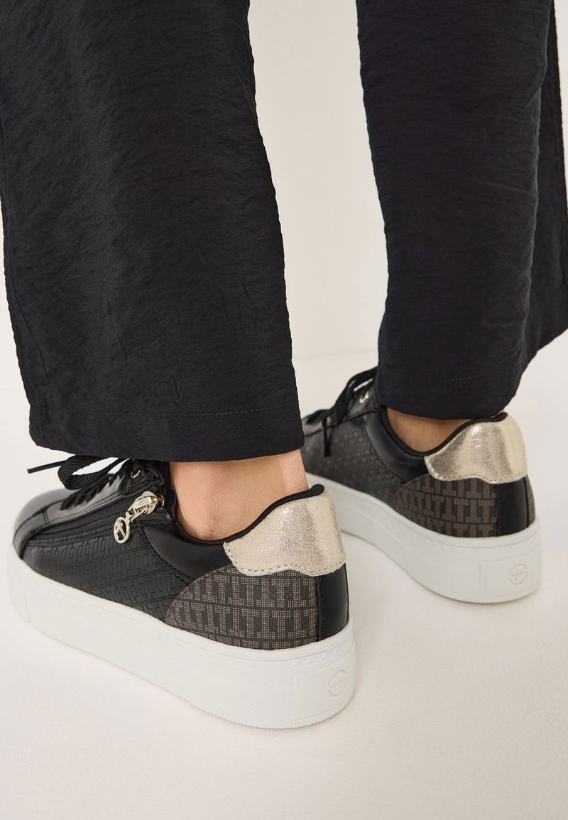 Sneaker neri e grigi con design testurizzato, accenti metallici dorati sul tallone e suola platform bianca. Inclusi lacci e dettaglio con zip.